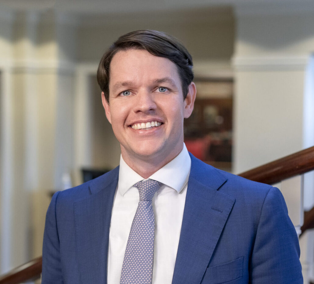 Cordon, a white man with brown hair, wears a blue suit, white shirt and blue tie.
