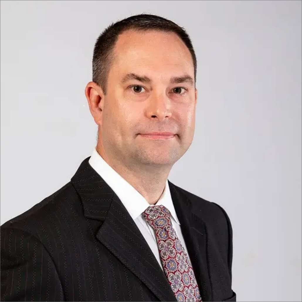 Chris, a white man with black hair, wears a white shirt, burgundy tie, and black suit.