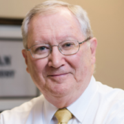 Ed, a white man with white hair and glasses, wears a white shirt and yellow tie.