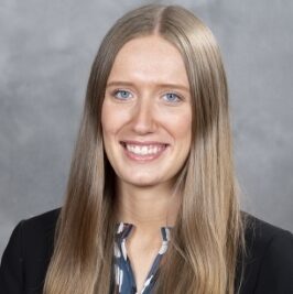 Emily, a white young woman with long blond hair, wears a blue and white blouse and black blazer.