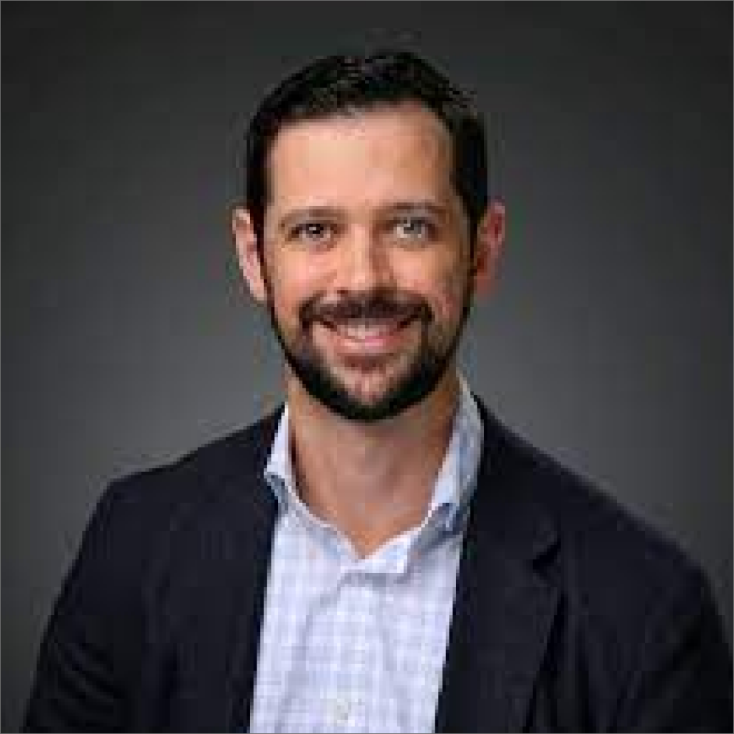 Troy, a white man with brown hair and a beard, wears a white and blue shirt and a black suit.