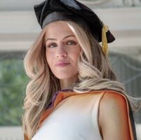 Isabella, a woman with blond hair, wears a white blouse and a graduation cap.
