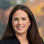 Kelsey, a white woman, wears a teal blouse and black suit.