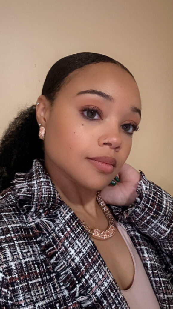 Mariah, a woman with black hair, wears a pink blouse and plaid blazer.