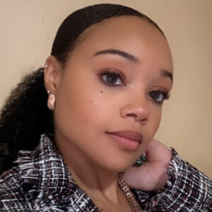 Mariah, a woman with black hair, wears a pink blouse and plaid blazer.