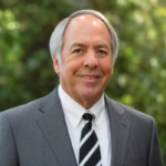 Robert, a white man with grey hair, wears a white shirt, black and white striped tie and grey suit.