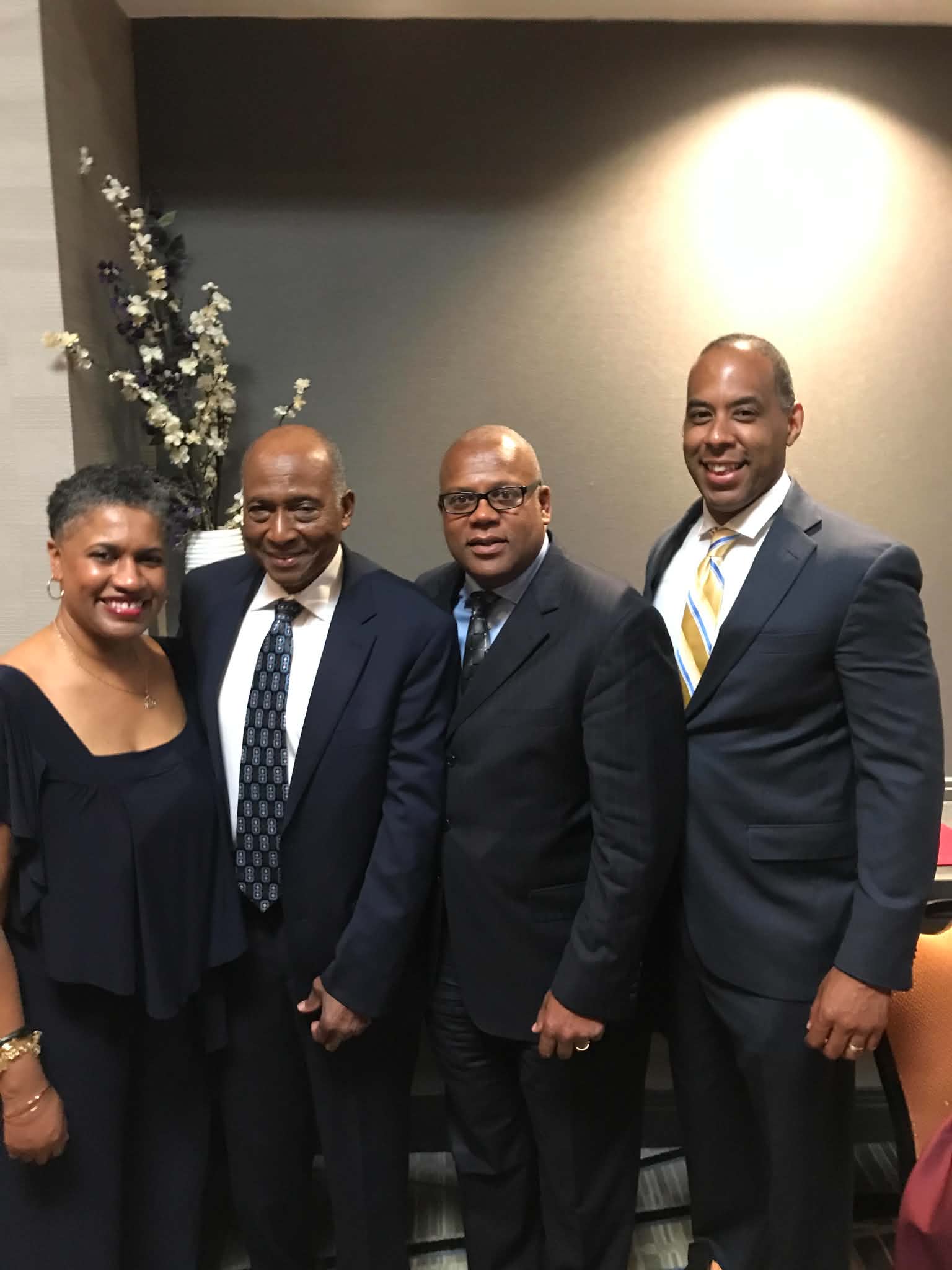 Kendall is a Black woman with black hair and she wears a black blouse. Smith is a Black man who wears a white shirt, dark tie and black suit. Springs is a Black man who wears a blue shirt, tie and black suit. Davis is a Black man who wears a white shirt, yellow tie and black suit.