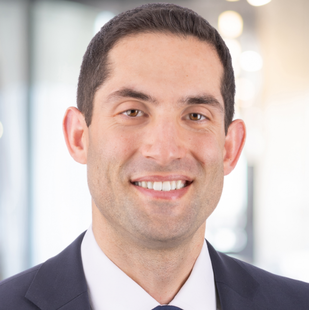 Daniel, a white man with brown hair, wears a white shirt, navy blue tie and dark grey suit.