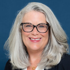 Jennifer, a white woman with gray hair and black glasses, wears a white blouse and black suit.