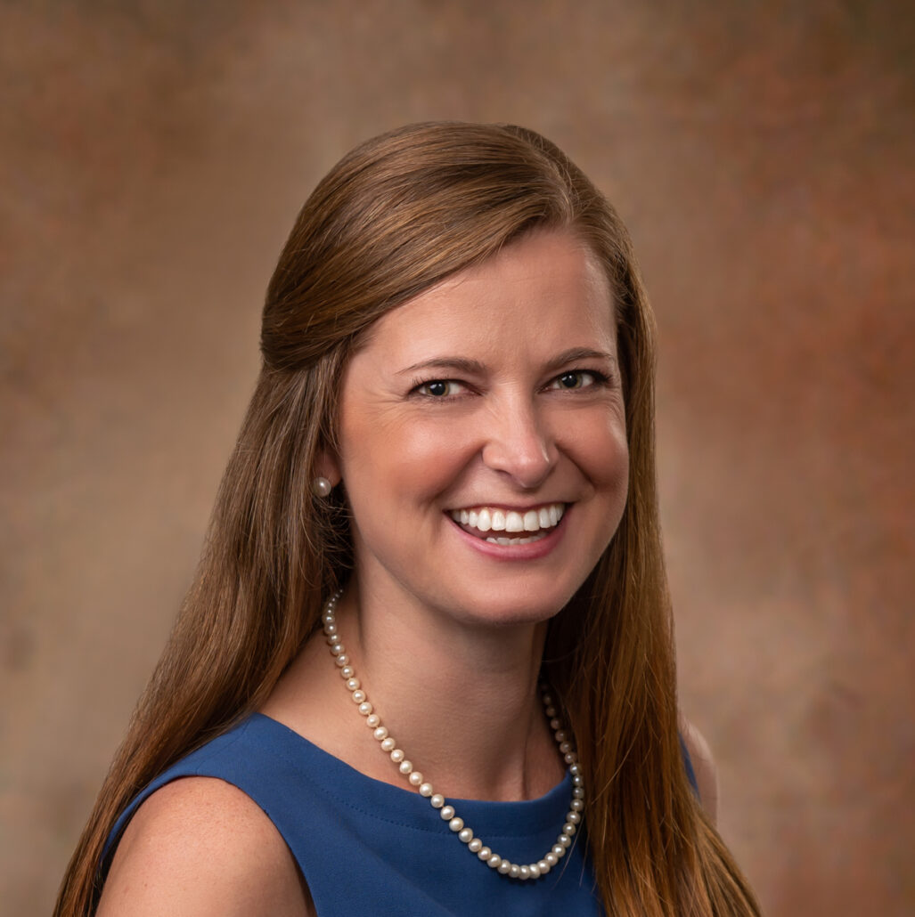 Alison, a white woman with auburn hair, wears a blue dress and pearl necklace.