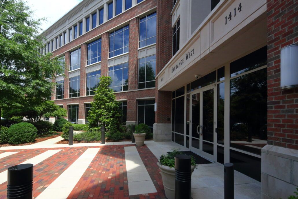 A four-story office building is shown, and the front is on the right-hand side. There are windows on the building and trees by the entrance. 