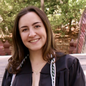 Kelsey, a white woman with brown hair, wears a black graduation gown.